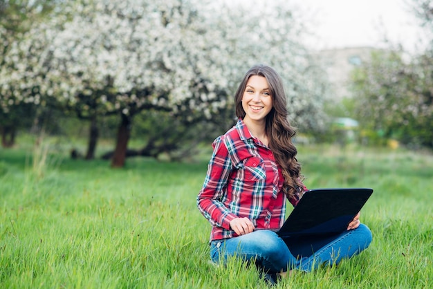 Young attractive woman with laptop on the grass in blooming garden