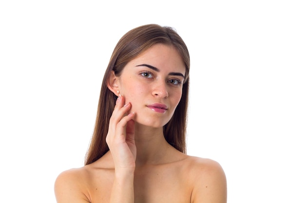 Young attractive woman with long brown hair touching her face on white background in studio