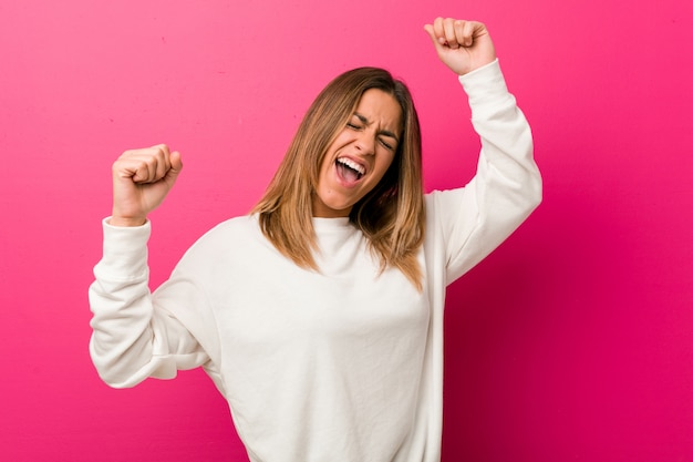 Young authentic charismatic real people woman against a wall celebrating a special day, jumps and raise arms with energy.