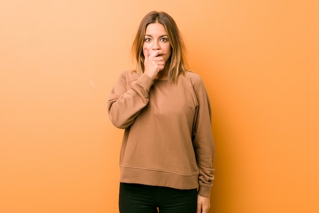 Young authentic charismatic real people woman against a wall thoughtful looking to a copy space covering mouth with hand.