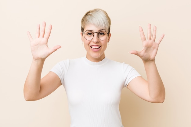 Young authentic natural woman wearing a white shirt showing number ten with hands.