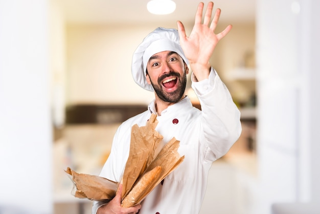 Young baker holding some bread and saluting in the kitchen