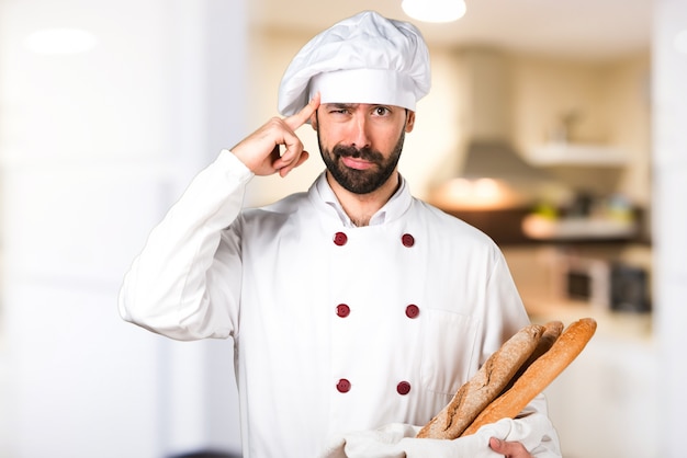 Young baker holding some bread and thinking in the kitchen