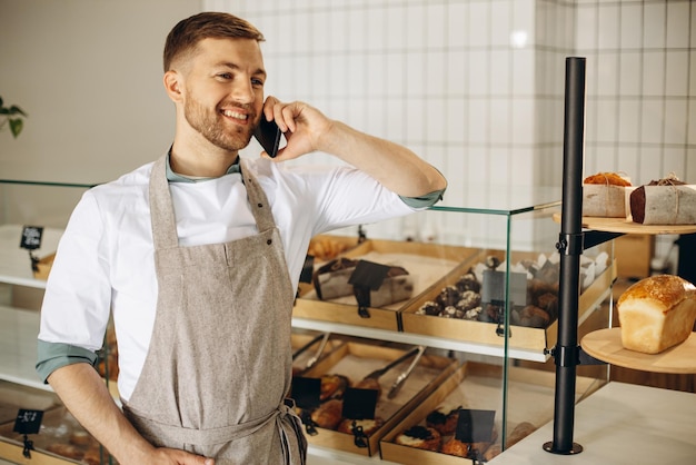 Young baker standing by the counter and talking on the phone