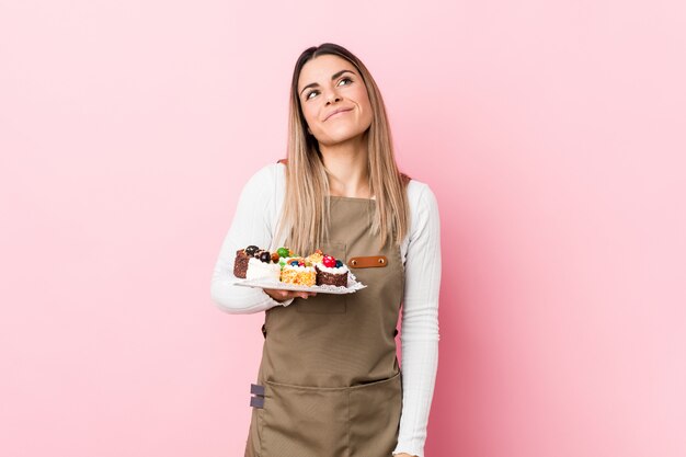 Young baker woman holding sweets dreaming of achieving goals and purposes