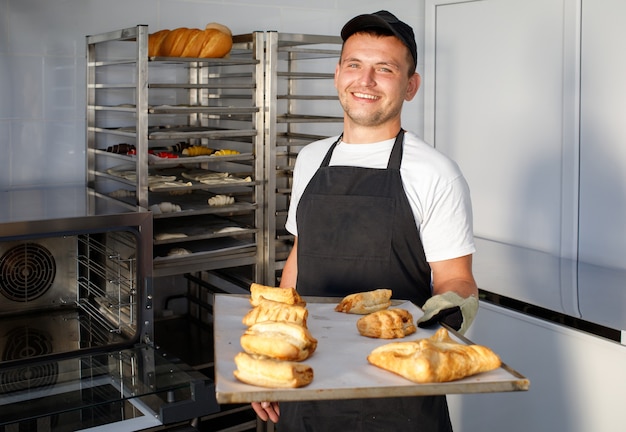 A young baker worker in a bakery is holding pastries