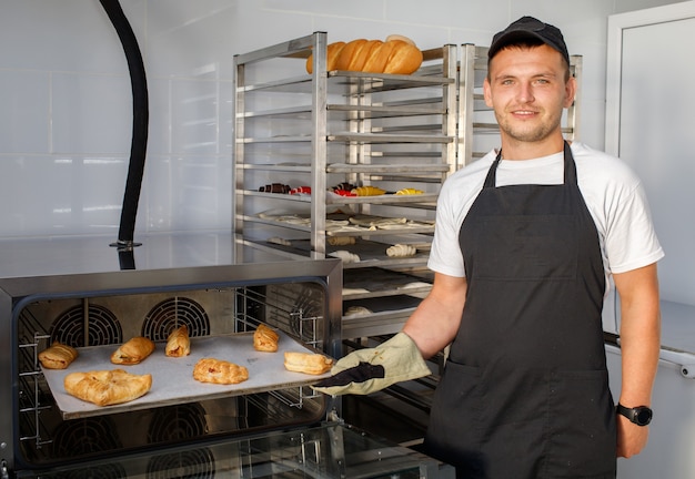 A young baker worker in a bakery is holding pastries