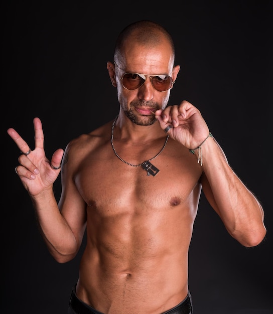 Young bald handsome man in sunglasses with naked torso on a dark background