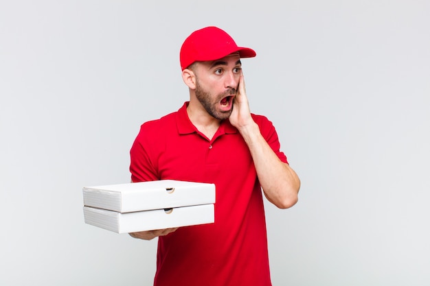 Young bald man feeling happy, excited and surprised, looking to the side with both hands on face