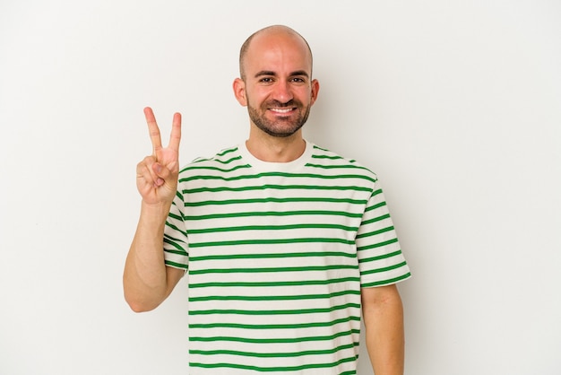 Young bald man isolated on white background joyful and carefree showing a peace symbol with fingers.