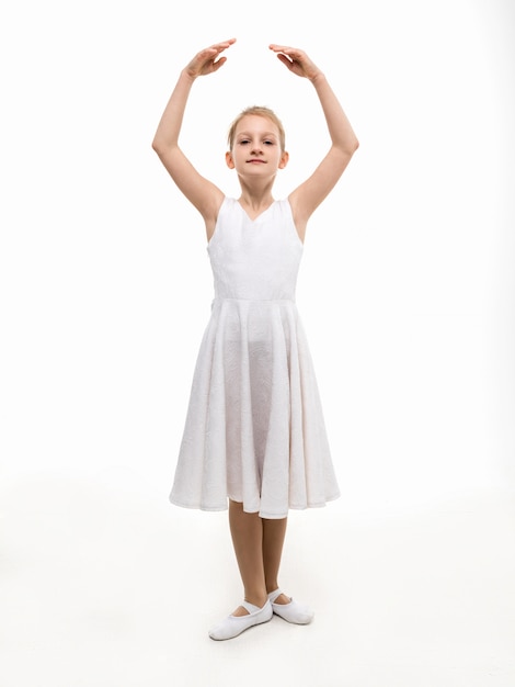 Young ballerina in a white dress stands in a dance pose on a white background