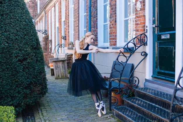 Young ballerina woman with red hair in ballet costume and pointe shoes is in beautiful pose dancing on street.