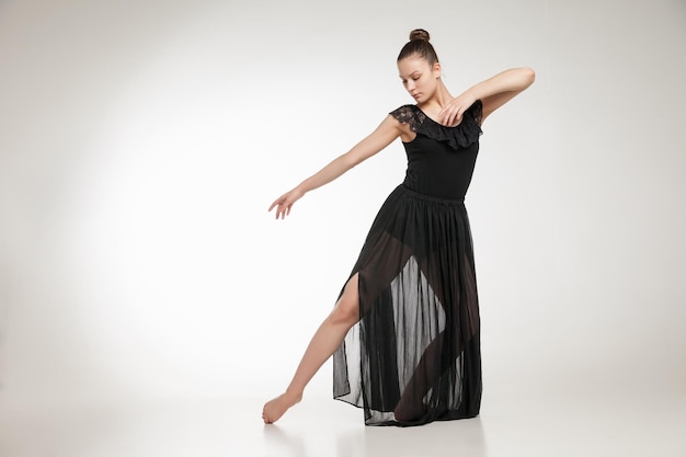 Young ballet dancer wearing black transparent dress dancing over white background