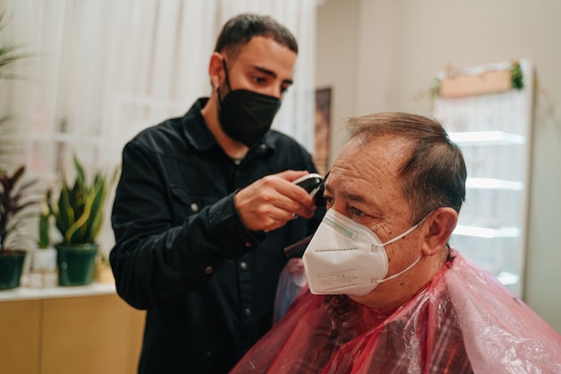 Young barber in his 30s cutting the hair of an older man in his 70s with a razor