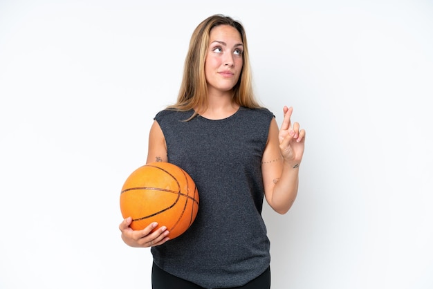 Young basketball caucasian player woman isolated on white background with fingers crossing and wishing the best