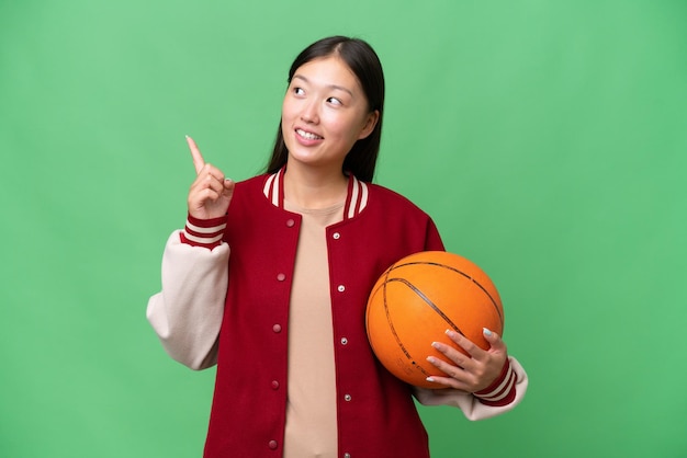 Young basketball player asian woman over isolated background pointing up a great idea