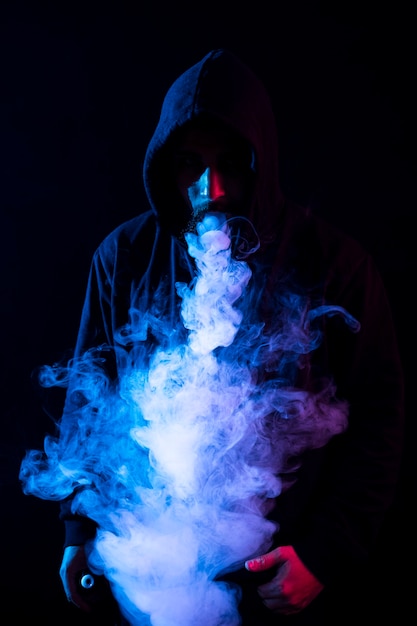 Young bearded arab man smoking vape and doing tricks with colored lights. Vertical