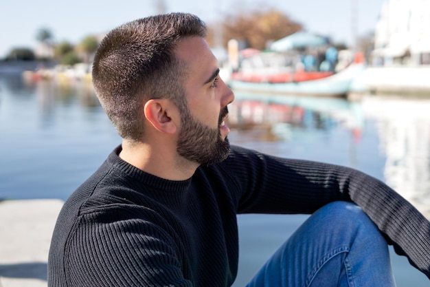 Young bearded boy in the foreground sitting in front of a canal with boats in Aveiro Portugal