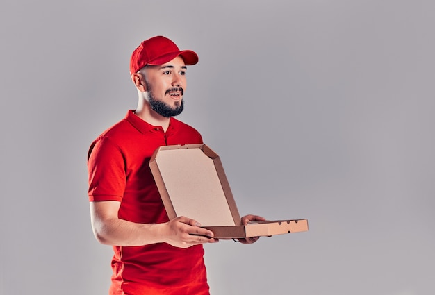 Young bearded delivery man with pizza box isolated on gray background.