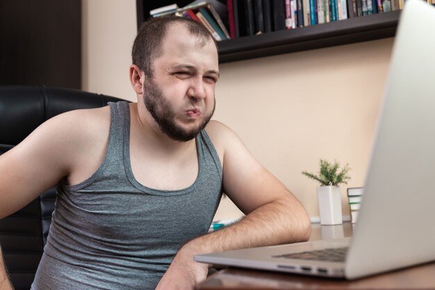 A young bearded guy in home clothes gray T-shirt, uses laptop