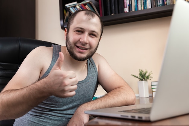 A young bearded guy in home clothes gray T-shirt, uses laptop