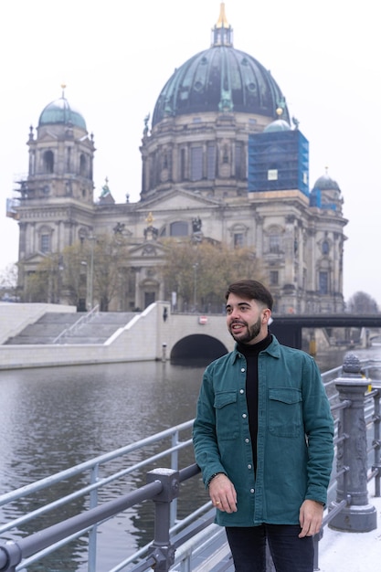 Young bearded male tourist leaning against the river fence with the Berlin Cathedral in the background Germany