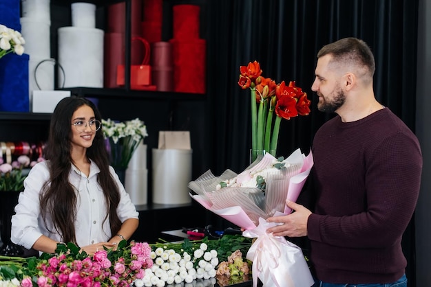 A young bearded man buys a beautiful bouquet of flowers for a girl's holiday in a cozy flower shop Floristry and bouquet making in a flower shop Small business