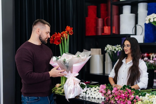 A young bearded man buys a beautiful bouquet of flowers for a girl's holiday in a cozy flower shop Floristry and bouquet making in a flower shop Small business