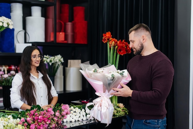 A young bearded man buys a beautiful bouquet of flowers for a girl's holiday in a cozy flower shop Floristry and bouquet making in a flower shop Small business