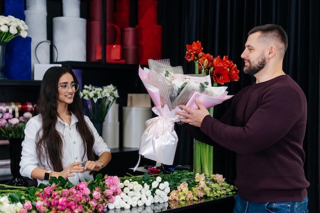 A young bearded man buys a beautiful bouquet of flowers for a girl's holiday in a cozy flower shop Floristry and bouquet making in a flower shop Small business