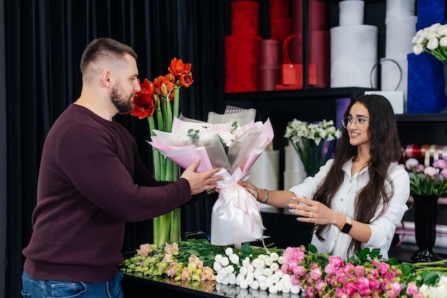 A young bearded man buys a beautiful bouquet of flowers for a girl's holiday in a cozy flower shop Floristry and bouquet making in a flower shop Small business