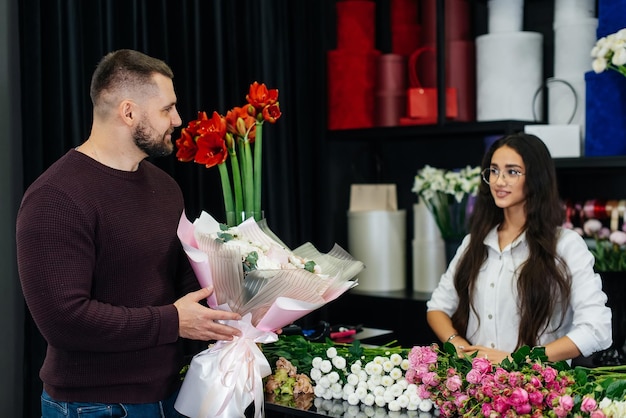 A young bearded man buys a beautiful bouquet of flowers for a girl's holiday in a cozy flower shop Floristry and bouquet making in a flower shop Small business