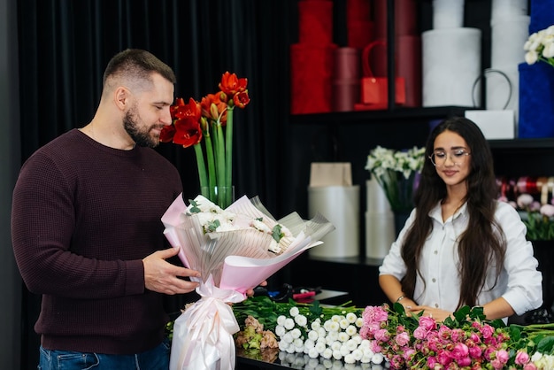 A young bearded man buys a beautiful bouquet of flowers for a girl's holiday in a cozy flower shop Floristry and bouquet making in a flower shop Small business