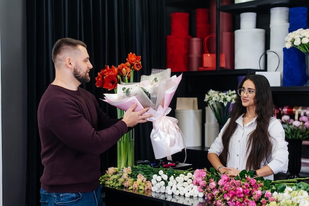 A young bearded man buys a beautiful bouquet of flowers for a girl's holiday in a cozy flower shop Floristry and bouquet making in a flower shop Small business