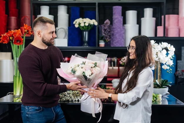 A young bearded man buys a beautiful bouquet of flowers for a girl's holiday in a cozy flower shop Floristry and bouquet making in a flower shop Small business