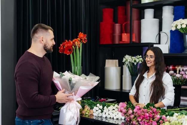 A young bearded man buys a beautiful bouquet of flowers for a girl's holiday in a cozy flower shop Floristry and bouquet making in a flower shop Small business