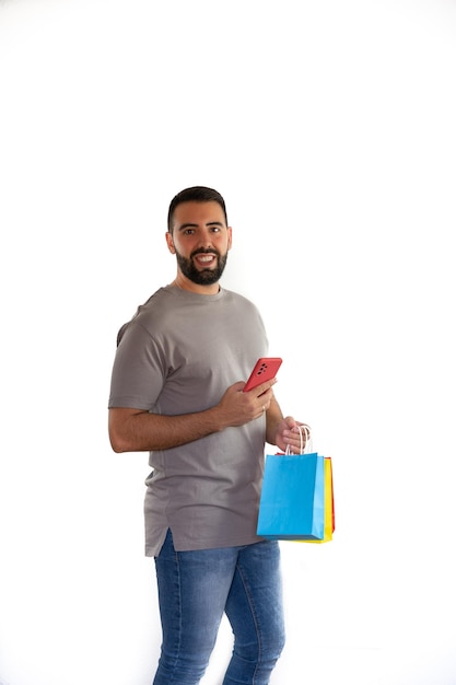 Young bearded man happily holding colorful bags and cell phone concept shopping black friday sales christmas