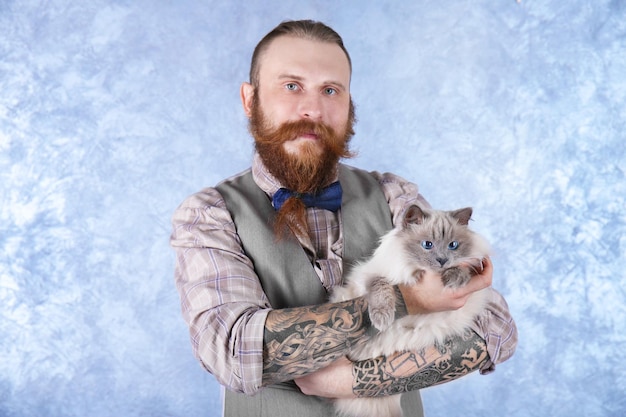 Young bearded man in plaid cap with fluffy cat on light background