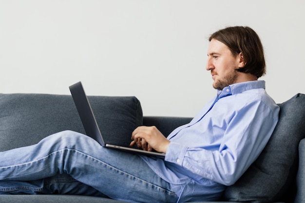 Young bearded man resting on a couch with a laptop