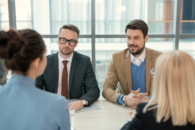 Young bearded man sitting with lawyer and discussing divorce papers with wife at meeting