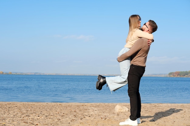 A young bearded man in sunglasses picked up a blonde girl The girl hugs the guy by the neck and laughs