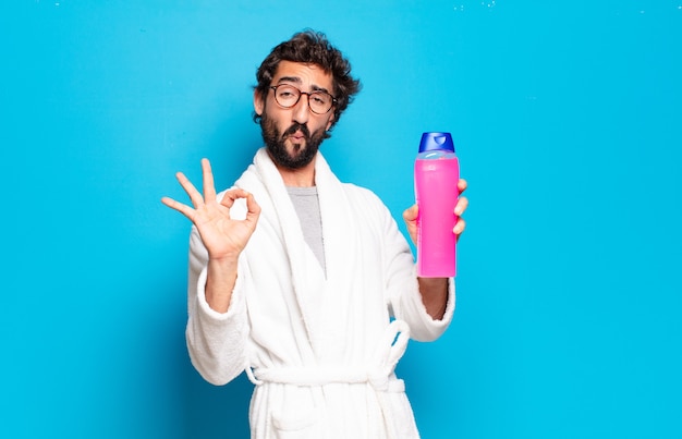 young bearded man wearing bathrobe with shampoo and beauty products