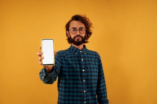 Photo young bearded young man with glasses showing mobile screen in white isolated on yellow background