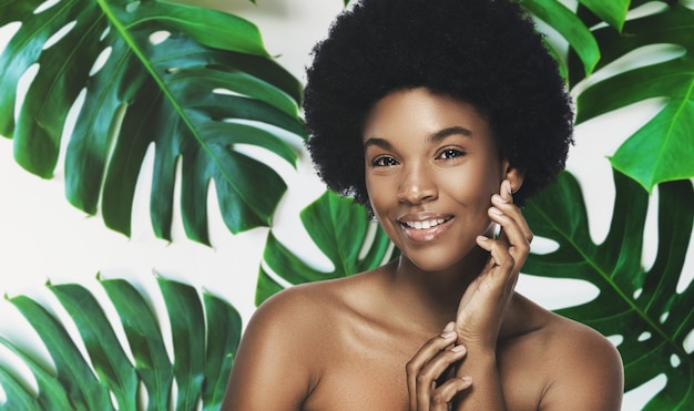 Young and beautiful African woman with perfect smooth skin in tropical leaves. Concept of natural cosmetics and skincare.