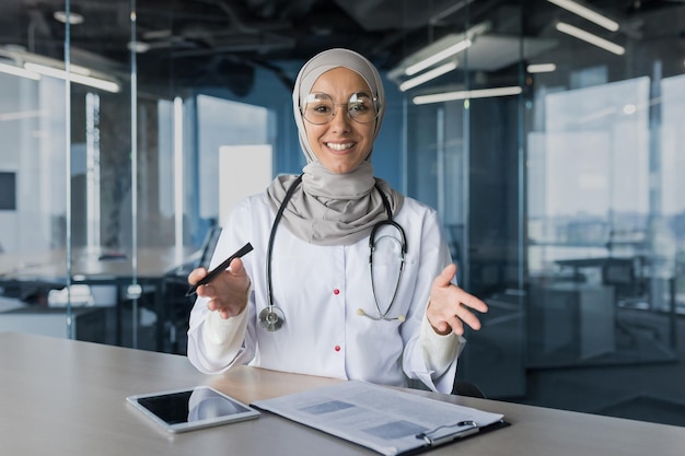 A young beautiful arab woman a muslim doctor is sitting in the office at the desk in a hijab