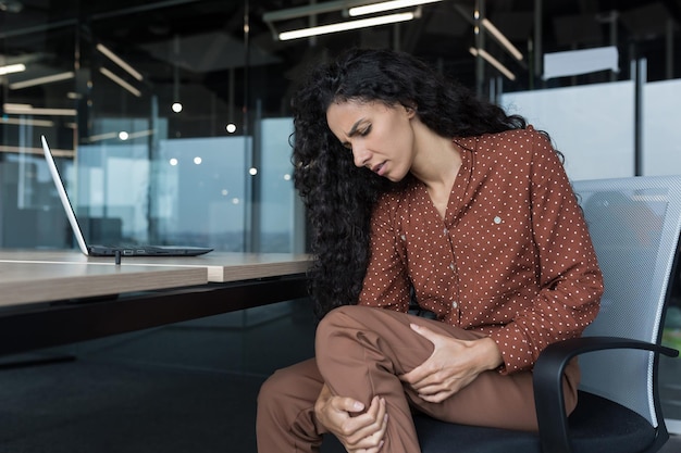 Young beautiful arab woman working in modern office with laptop curly business woman has severe pain