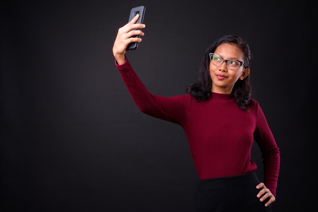  young beautiful Asian businesswoman with nose ring against black wall