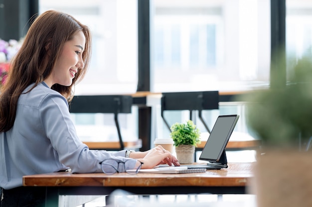 Young beautiful asian businesswoman working on tablet with happiness while sitting at the table in modern office room.