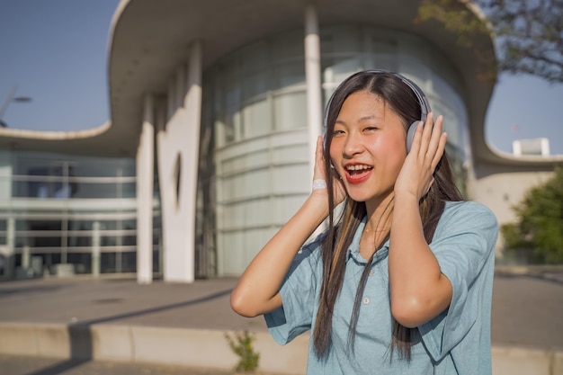 Young beautiful asian girl with headphones happy smiling and dancing in the street