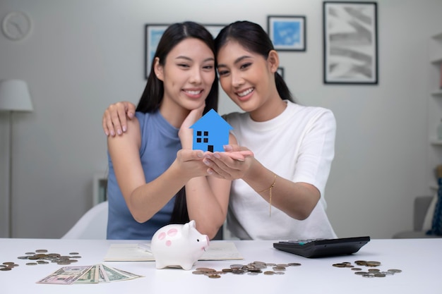 Young beautiful Asian lesbian couple saving money to buy a house LGBT women couple saving money for family and home Focus on toy house